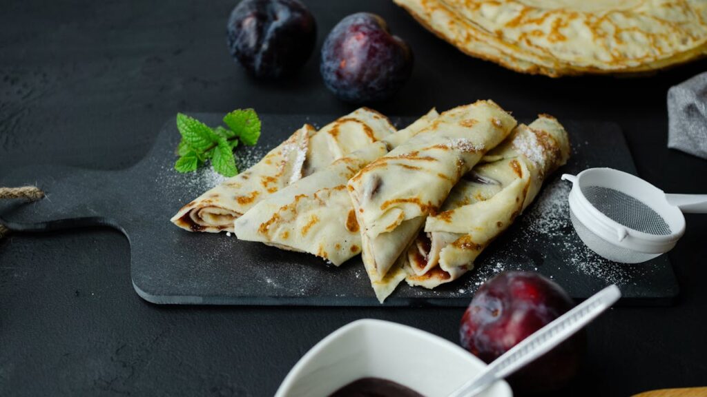 pexels-photo-13427907 Delicious homemade crepes filled with jam and fresh plums on a serving board.