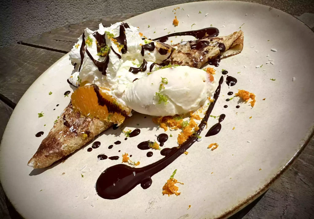 Crêpe dorée et croustillante servie dans une assiette rustique, garnie de fruits frais, d’un filet de chocolat fondant et d’une boule de glace vanille. Une spécialité gourmande de la crêperie Léon et Suzette à Moncoutant-sur-Sèvre, à seulement 15 minutes de Bressuire.
